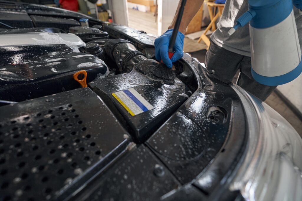 Washing car engine with wash foam in repair shop